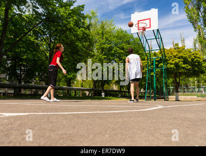 Jeune couple athlétique jouant au basket-ball ensemble sur cour en plein air, dans un parc verdoyant Banque D'Images