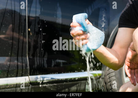 Close Up of Man Washing car, accroupi à côté de voiture noir et bleu à l'extérieur d'une éponge savonneuse Squeezing Banque D'Images