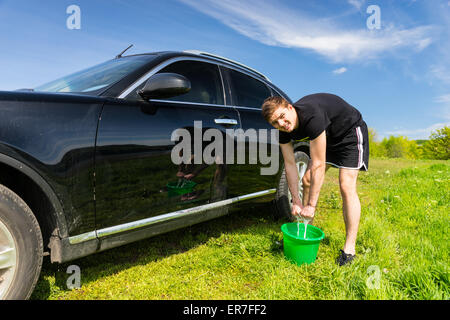 L'homme à la caméra et à l'essorage de l'Éponge savonneuse dans la benne verte pendant le lavage de véhicules de luxe noir en vert les champs o Banque D'Images