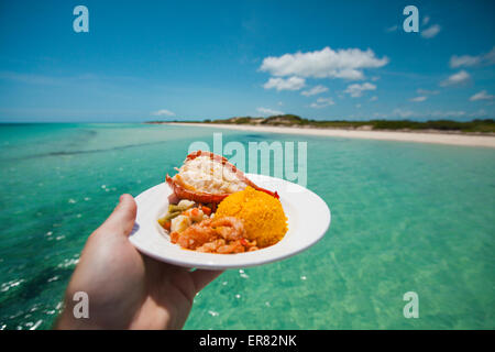 Un homme est titulaire d'un plateau de fruits de mer avec crevettes, queue de homard, et tandis que le riz assaisonné sur un bateau Banque D'Images