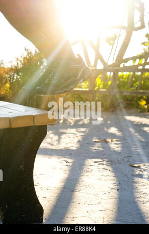 Les jambes de quelqu'un sautant vers le haut sur un banc de parc Banque D'Images