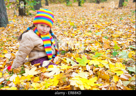 Jeune fille s'asseoir sur des feuilles jaunes en automne park Banque D'Images