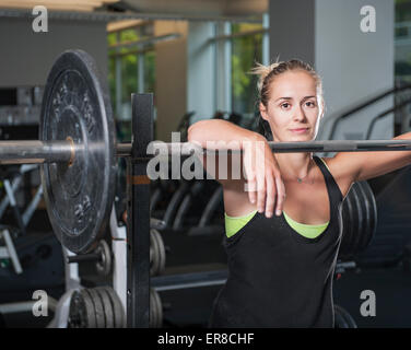 Portrait of woman leaning on barbell at gym Banque D'Images