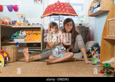 Portrait of happy mother with daughter holding umbrella, assis sur plancher de bois franc dans les Banque D'Images