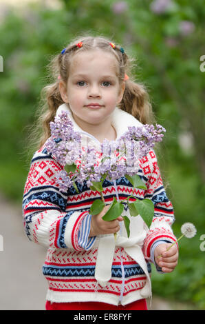 Half-length portrait jeune fille de quatre ans dans une veste avec un bouquet de lilas et un pissenlit en mains Banque D'Images