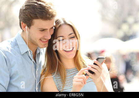 Couple heureux avec vos écouteurs le partage de la musique à partir d'un téléphone intelligent dans la rue Banque D'Images