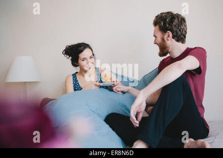 Portrait of happy young woman holding birthday cupcake avec bougie allumée sur l'homme assis à côté de bed Banque D'Images