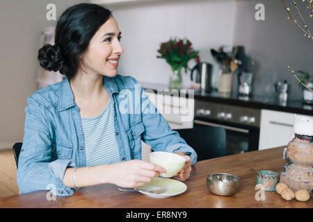 Happy young woman having coffee tout en regardant ailleurs dans la cuisine Banque D'Images