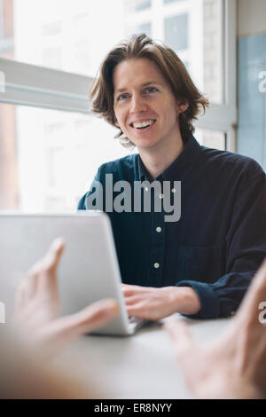 Jeune homme souriant à collègue while using laptop at table Banque D'Images