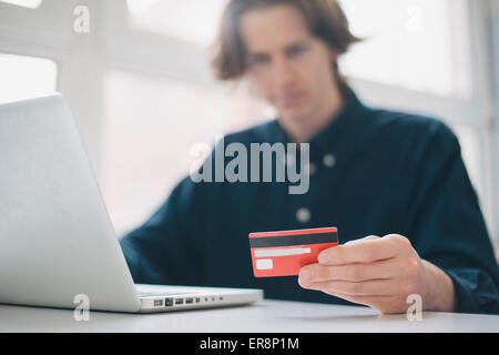 Jeune homme tenant une carte de crédit lors de l'utilisation d'ordinateur portable sur un bureau Banque D'Images