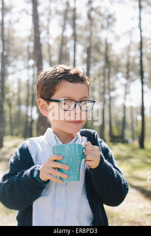 Boy holding coffee mug in forest Banque D'Images