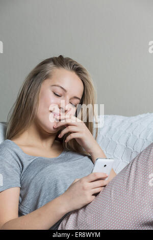 Teenage girl using smart phone on sofa at home Banque D'Images