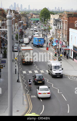 Voitures, camions et les cyclistes sur Lee Bridge Road, une banlieue animée high street, dans le nord de Londres. London city skyline en arrière-plan Banque D'Images