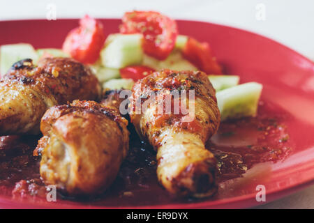 Cuisses de poulet rôti bio faits maison avec des épices servi sur assiette rouge Banque D'Images
