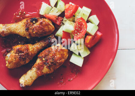 Cuisses de poulet rôti bio faits maison avec des épices servi sur assiette rouge Banque D'Images