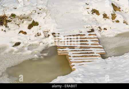 Petite passerelle en bois sur de petits cours d'eau gelés à la fin de l'hiver. Banque D'Images