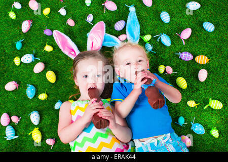 Enfants sur chasse aux œufs de Pâques. Les enfants mangent lapin en chocolat. Garçon et fille se détendre sur une pelouse verte dans le jardin. Banque D'Images