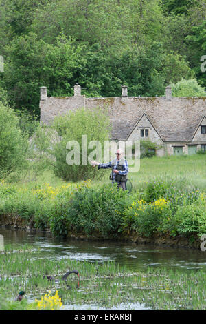 L'homme pêche de mouche sur la rivière Coln en face de Arlington row, Bibury, Cotswolds, Gloucestershire, Angleterre Banque D'Images
