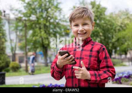 Petit garçon enfant kid jouer à des jeux sur téléphone mobile smartphone à l'extérieur. Génération technologique. Banque D'Images