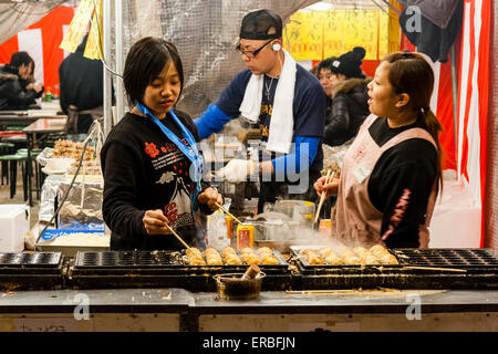 Deux femmes japonaises discutant l'une avec l'autre pendant la cuisson de takoyaki, des boules de poulpe, sur des plaques chauffantes spécialement faites sur le stand de nourriture à l'heure de la nuit. Banque D'Images