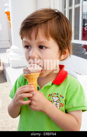 Enfant, garçon, 3 à 4 ans, extérieur, tenant le cône de glace dans les deux mains et se mordant au bord du cône et de la glace. Tir sur la tête et l'épaule. Banque D'Images