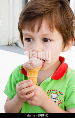 Enfant, garçon, 3 à 4 ans, extérieur, tenant le cône de glace dans les deux mains et se mordant au bord du cône et de la glace. Tir sur la tête et l'épaule. Banque D'Images