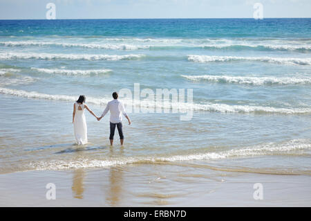 Bride and Groom holding hands marche sur la plage de sunny day Banque D'Images