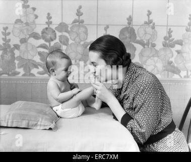 1930 FEMME Mère embrassant les pieds de bébés Banque D'Images