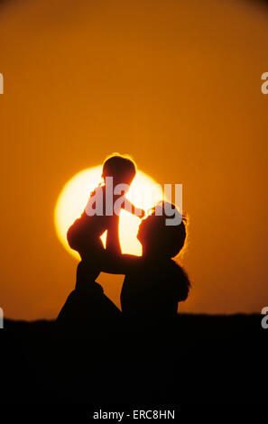 La silhouette ANONYME MOTHER HOLDING BABY EN L'AIR AU COUCHER DU SOLEIL Banque D'Images