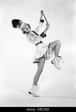 1960 FEMME MAJORETTE UNIFORME jupe courte bande BOOTS GLANDS MARCHER UNE DEBOUT HOLDING BATON SMILING Banque D'Images