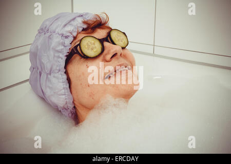 Femme mature dans une baignoire avec des tranches de concombres sur des verres, retro style Banque D'Images