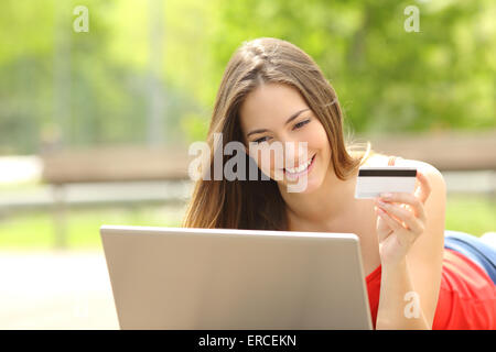 Fille de l'acheteur l'achat en ligne avec un ordinateur portable et une carte de crédit se trouvant dans un parc en été Banque D'Images