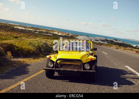 Jeune couple roulant dans une voiture sur une route ouverte avec ciel bleu et mer en arrière-plan. Jeune couple on road trip sur journée d'été. Banque D'Images