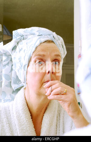 Middle aged woman faire composent dans la chambre au miroir de coiffeuse indésirables de fraisage avec des ciseaux poils du nez Banque D'Images