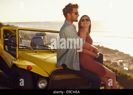 Portrait de couple assis sur le capot de leur voiture avec couple et profiter de la vue en femme lo Banque D'Images