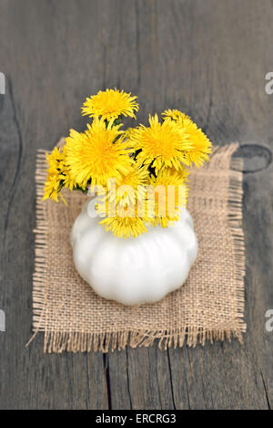 Bouquet de pissenlits en vase en céramique blanche sur table en bois Banque D'Images