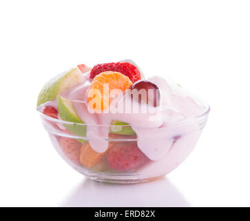 Salade de fruits colorés dans un bol en verre, garni de yogourt aux fraises rose, sur un fond clair Banque D'Images