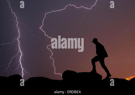 Silhouette d'un homme qui marche au sommet d'une montagne, avec la foudre dans le ciel Banque D'Images