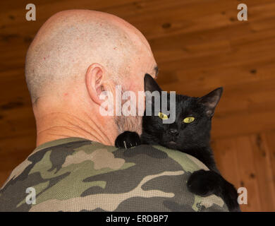 Homme d'âge moyen avec son chat noir regardant par-dessus son épaule au viewer Banque D'Images