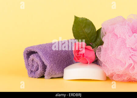 Avec du savon rose rose à côté d'une douche puff et laver chiffon contre la lumière fond jaune Banque D'Images