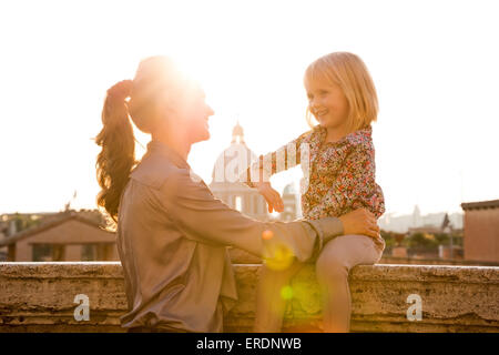 Au coucher du soleil, une brunette mère de profil, il est souriant et à parler à sa fille blonde qui est assise sur un rebord au-dessus de la cit Banque D'Images