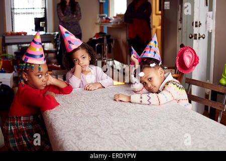 Les enfants s'ennuyer wearing party hats at table Banque D'Images