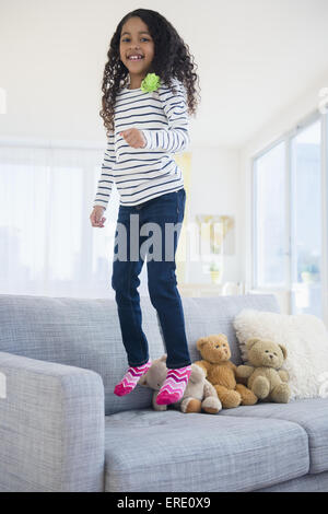 Mixed Race girl jumping on sofa Banque D'Images