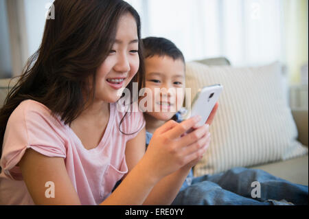 Frère et soeur asiatique using cell phone on sofa Banque D'Images