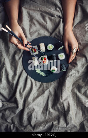 Woman eating sushi avec des baguettes au lit Banque D'Images