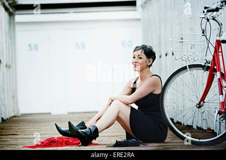 Older Caucasian woman sitting with bicycle on wooden dock Banque D'Images