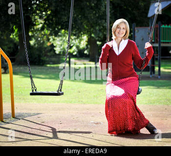 Une femme en rouge s'assit sur une balançoire dans un parc. Banque D'Images