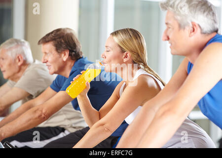 Une femme assoiffée de boire le jus d'orange dans la salle de sport sur spinning bike Banque D'Images