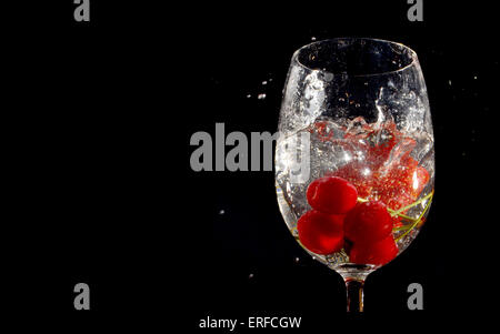 Les cerises et les fraises ont chuté en verre d'eau isolées sur fond noir Banque D'Images