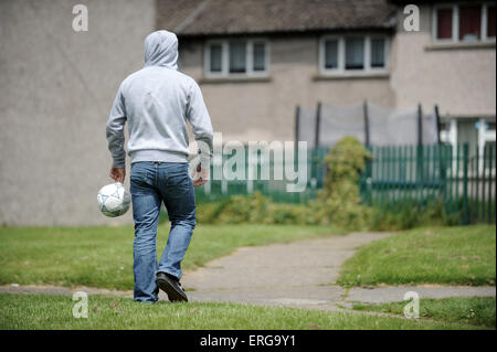 Un homme porte une jeunesse au football sur une course vers le bas sur le Gurnos estate dans Merthyr, Galles du sud. Banque D'Images